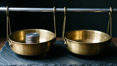 Two brass pans hang from hooks on a steel bar and rest on dark slate, the left one holding a short stack of grey metal discs and the right one empty.