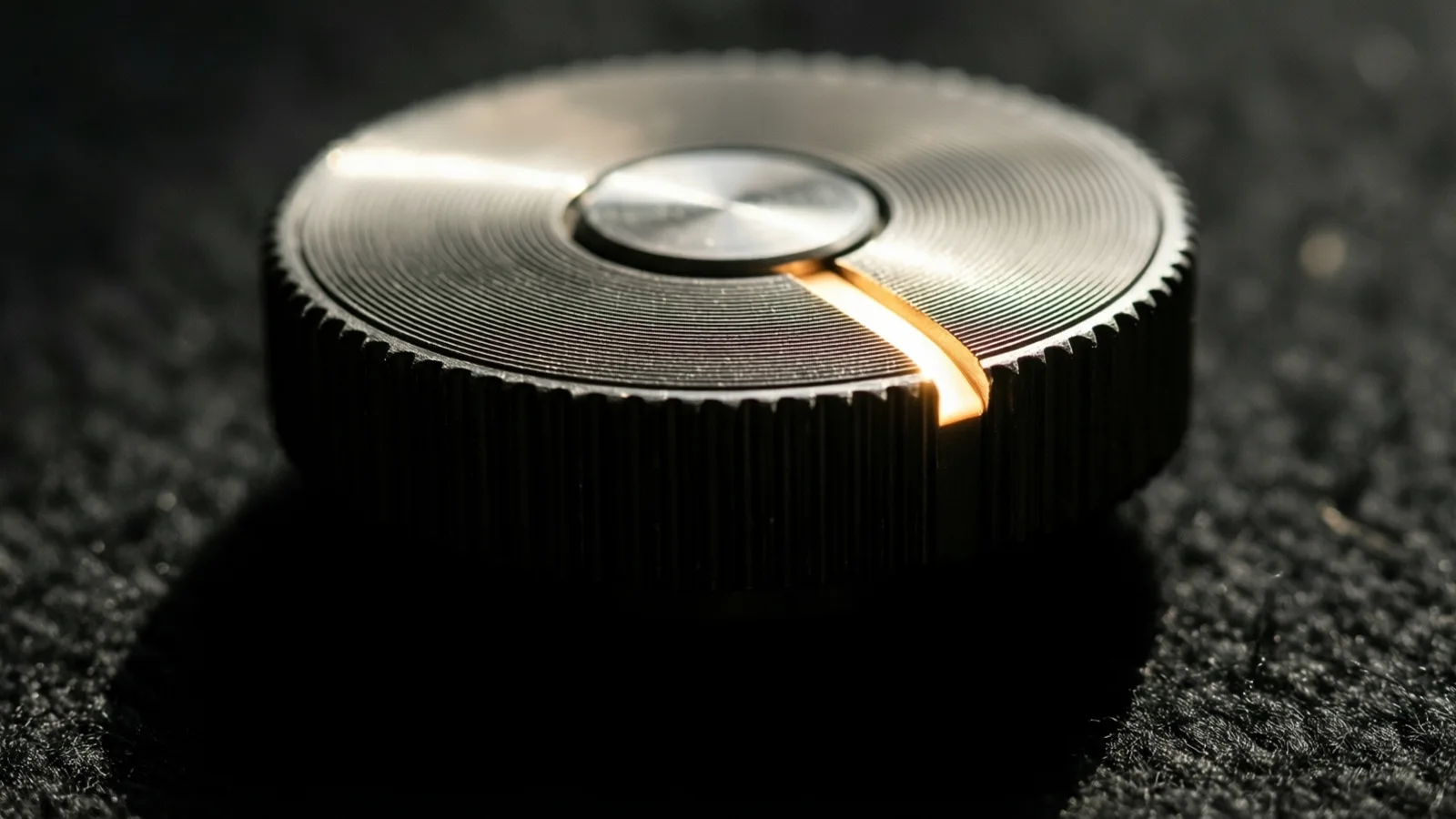 A grooved metal wheel resting on dark felt, one ridge catching a warm line of light against deep black shadow.