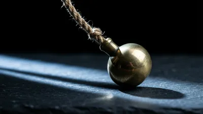 Una plomada de latón pulido descansa sobre una losa de pizarra oscura, con la cuerda de fibra deshilachada subiendo hacia la esquina superior izquierda, mientras una franja de luz fría cruza la piedra y proyecta una sombra larga detrás.