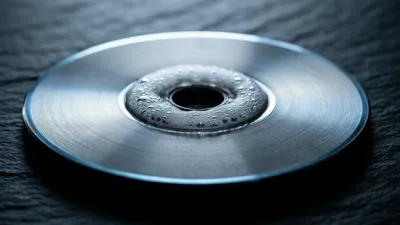 Sobre pizarra oscura descansa un disco redondo de acero, con un anillo de condensación que empaña su centro bajo una fina franja de luz fría.