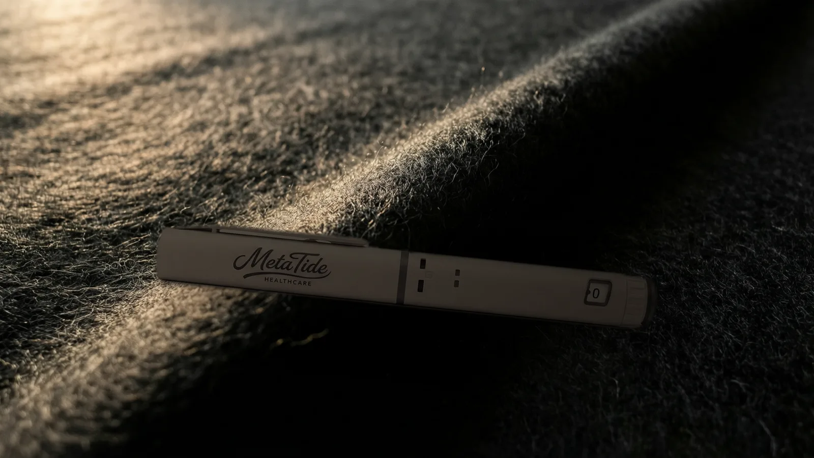 A prefilled multi-dose research pen resting across a soft fold of thick charcoal felt in warm low light.