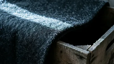 Heavy dark felt draped over a crate edge, its surface dusted with frost and lit by one cold blade of light.