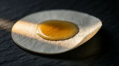 Un disco de papel de filtro sobre piedra oscura con una mancha pálida que se extiende desde el centro hacia afuera, bajo una única luz cálida.