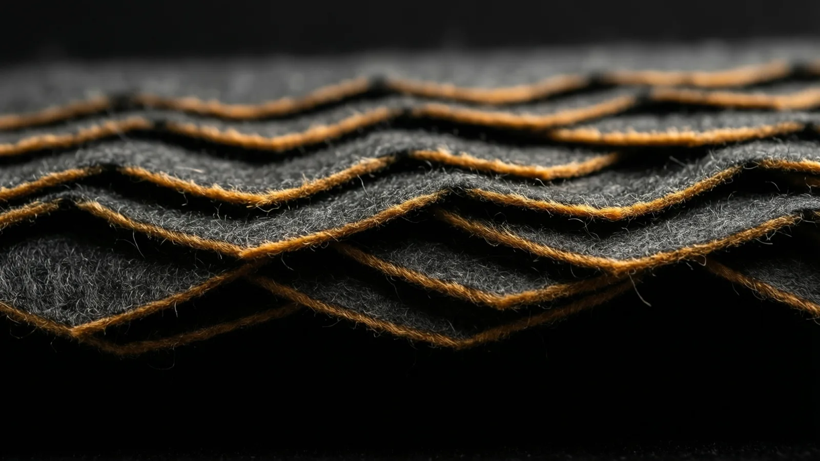 Overlapping pleated strips of dark felt layered like scales, warm light tracing a sliver along each ridge.