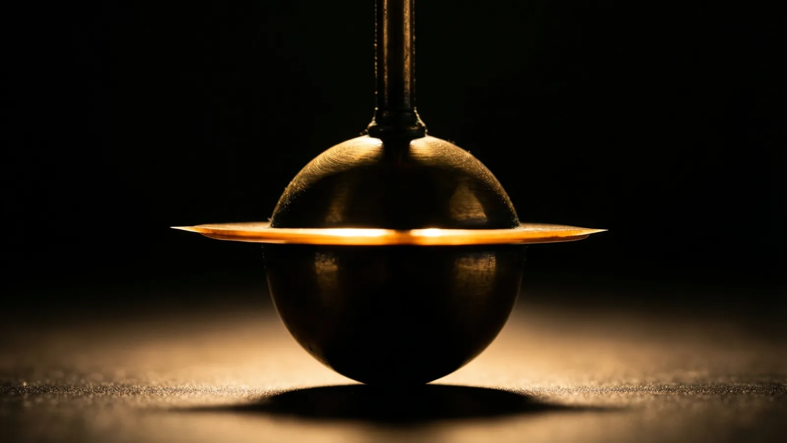 La lenteja de latón de un péndulo cuelga completamente inmóvil entre sombras densas, con una fina hoja de luz cálida que le cruza la parte más ancha.
