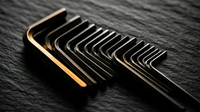 A fanned set of steel hex keys of graduated sizes rests on dark slate, one warm band of light tracing their polished edges.