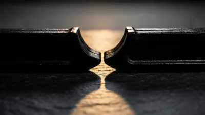 Two black spring clamps face jaw to jaw on dark slate, a warm band of light dividing the gap between them.