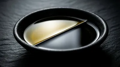 A shallow dark dish holds oil and water in separation, divided by a sharp bright boundary line.