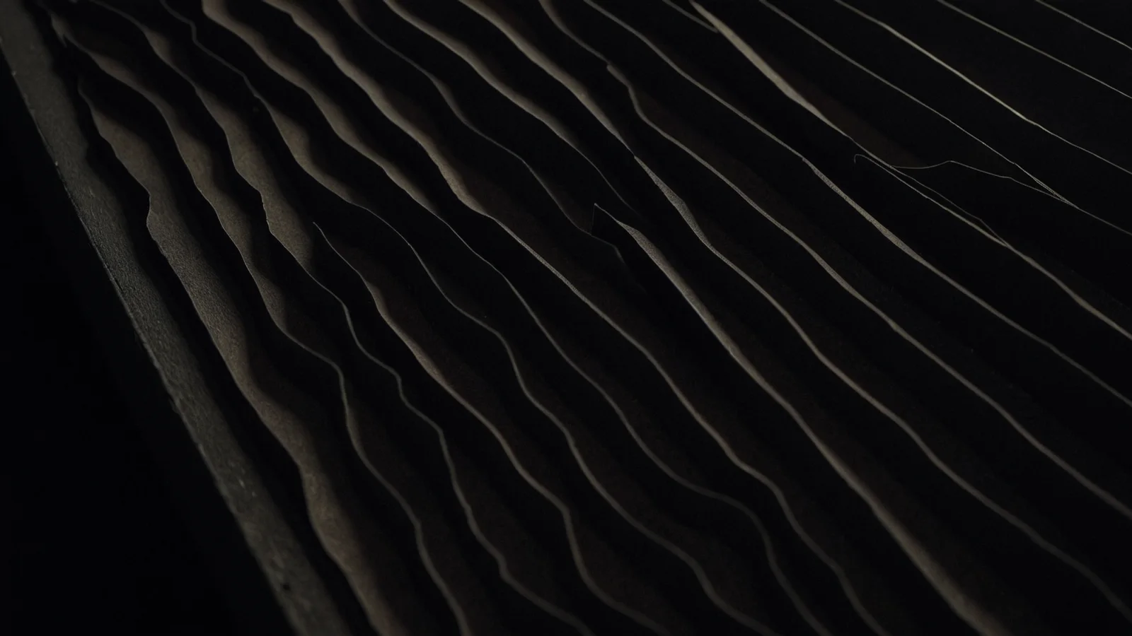 The edges of a long drawer of blank cards seen close up, forming a fine wavy ridge pattern under raking light.
