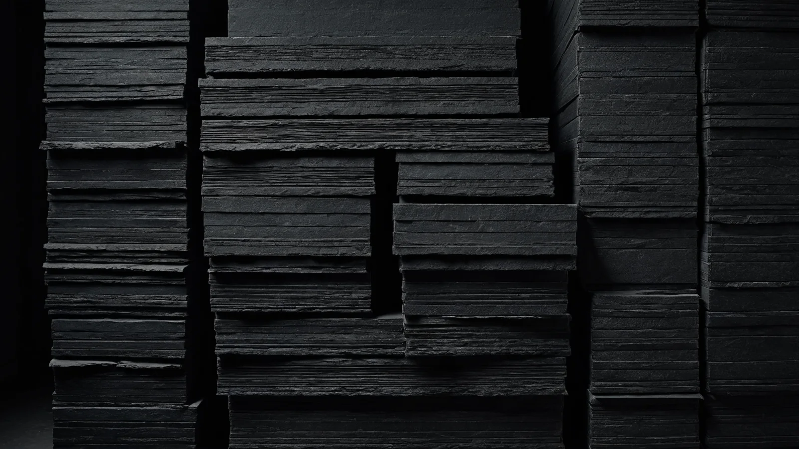 A column of stacked dark archive slabs on slate, one narrow band of light across their clean front edges.