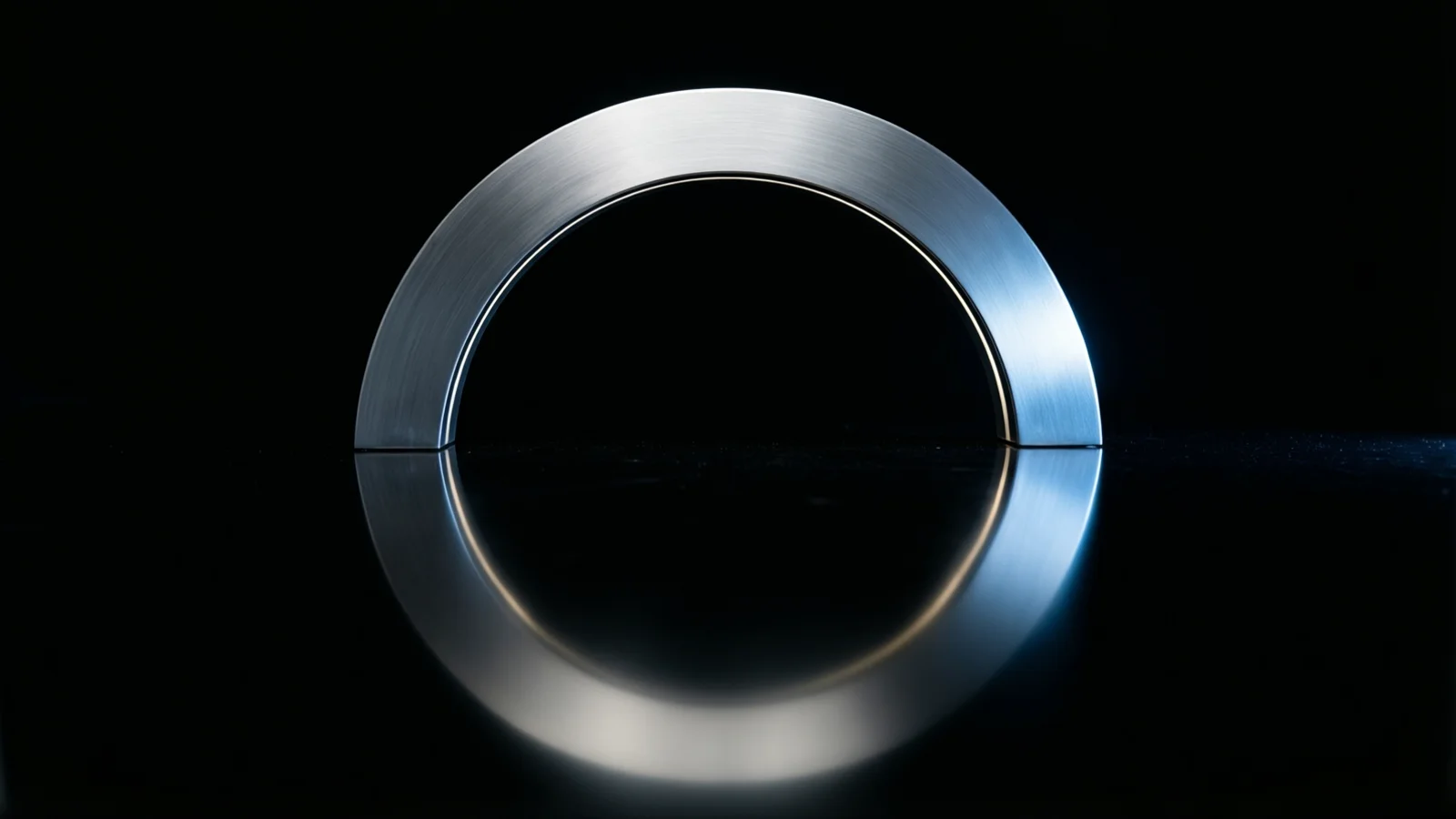 Una banda curva de metal cepillado forma un arco sobre una superficie negra brillante, y su reflejo debajo completa el círculo. Una luz de tono azulado incide en el lado derecho del metal, con fondo negro.