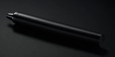 A single matte-black cylindrical dose pen lying on dark felt, wrapped in deep protective shadow with one soft edge of light tracing part of its silhouette.