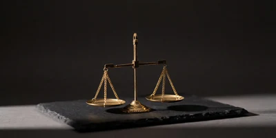 A small polished brass balance scale in near-perfect equilibrium on dark slate, its two empty pans level under a single band of warm light.