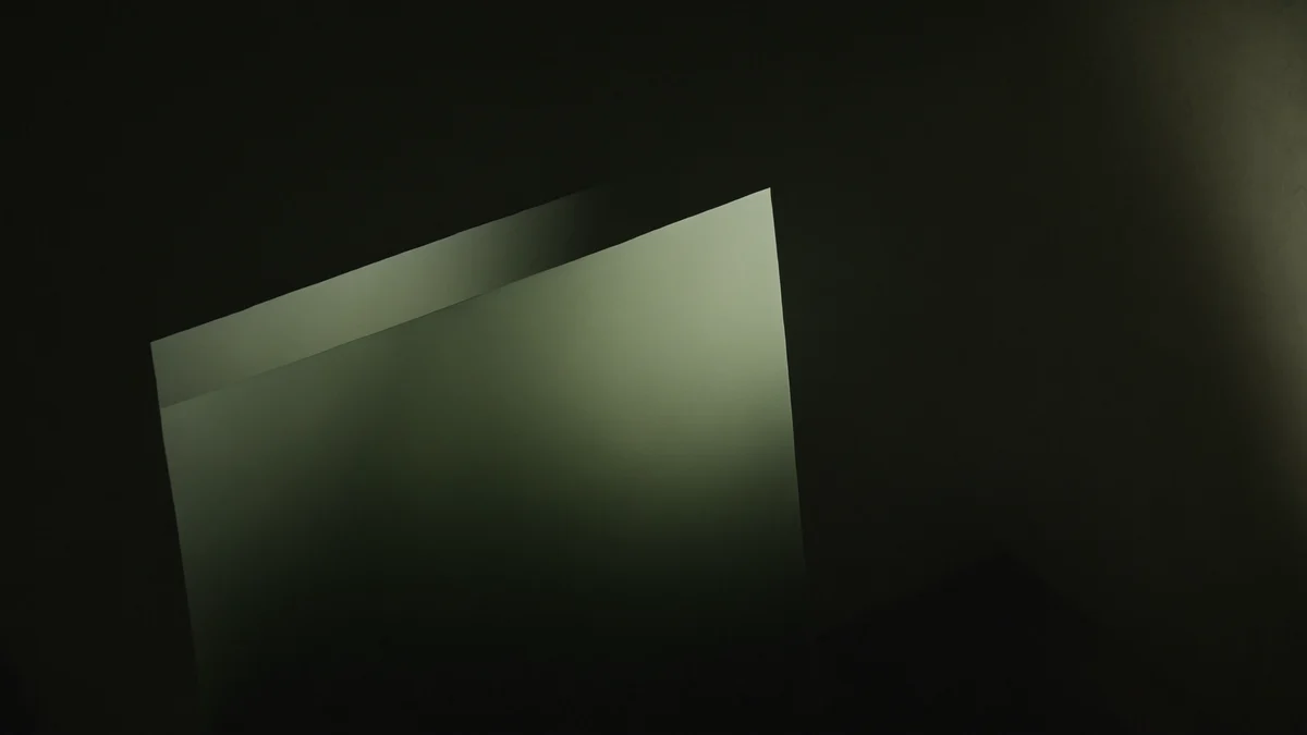 A translucent pale green film held against a dark background, its edges glowing where the light passes through.
